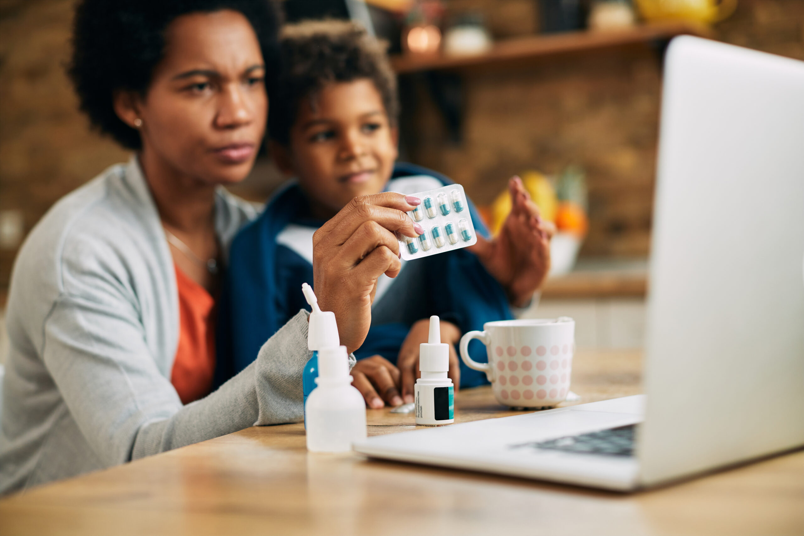 Close-up of African American mother having video call with family doctor and consulting about pills for her ill son.